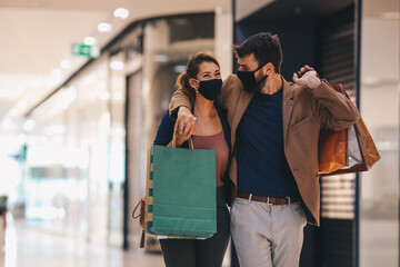 Fototapeta premium The young couple carries shopping bags and walks through the mall, wearing protective masks, life in a time of pandemic