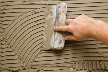 Worker hand using spatula and putting glue on wall for gluing ceramic tiles. Closeup.
