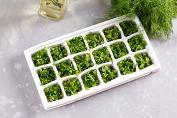 Ice cube tray with herbs frozen in oil and fresh herbs on light background. Top view.