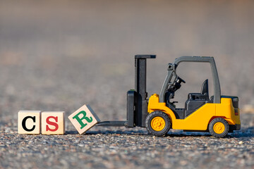 A toy forklift lifts a block with the letter R in CSR (abbreviation for corporate social responsibility) from the asphalt.