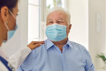 Happy senior white-haired patient in medical face mask trusting his young doctor