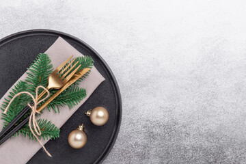 Fototapeta na wymiar Christmas table setting with black ceramic plate, gifts and fir tree branch on stone background. Top view. Copy space