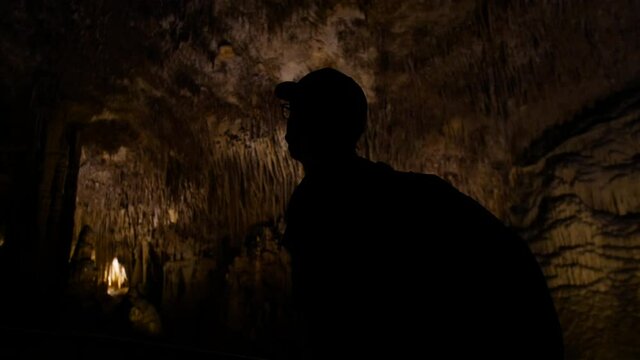 Man walking in low key overlooking cave's iluminated roof.
High angle, traveling movement, 4k 60p.