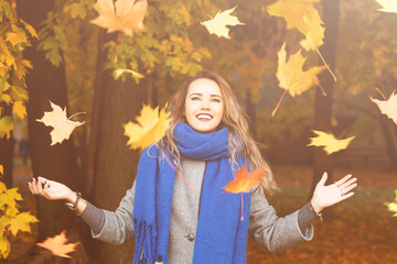 Outdoors lifestyle fashion image of happy beautiful girl throwing leaves up in the air in autumn...