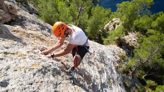Man lead climbing in nature rock and cliping the next quickdraw, next to sea, in Andratx coastline, Mallorca island, Spain.
Low angle, twist movement, 4K 60p.