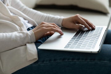 Close up of female relax on sofa typing texting on modern laptop, hands on keyboard. Young woman busy using computer, browsing surfing wireless internet, working online on device.