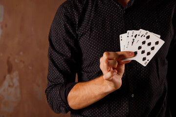 Close-up portrait of young man with gambling cards. Handsome guy shows tricks with card. Clever hands of magician on metal texture background. Concept of entertainment and Hobbies. Copyright space