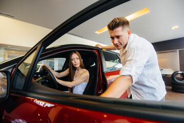 A happy young couple chooses and buys a new car at a car dealership. Buying a new car