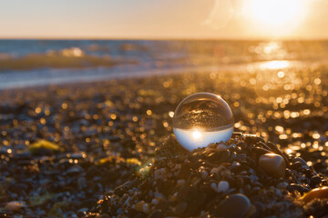 Glass round ball on the beach reflects the sea in summer at sunset