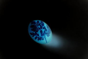 Easter egg in cyan color on a black background. Floral pattern on a luminous egg.