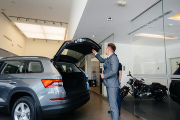 A young businessman with a salesman examines the trunk of a new car in a car dealership. Buying a car