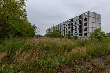 An abandoned multi-storey building stands in the middle of a green field. Multi-storey building without windows