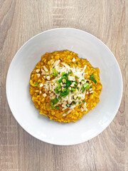 Close up of creamy orange pumpkin risotto in the white plate on wooden table. Spring onion, parmesan cheese and nuts on top. Home cooking.