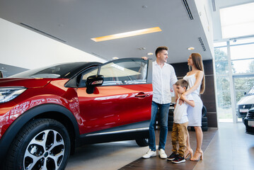Fototapeta na wymiar A happy young family chooses and buys a new car at a car dealership. Buying a new car
