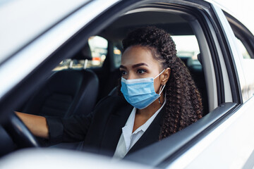 Young woman taxi driver sits in a car behind the steering wheel and driving during the covid-19 quarantine. Business trips during pandemic, new normal and coronavirus travel safety concept.