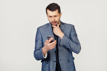 Young businessman man with a beard in a jacket using a smartphone scared shocked with a surprised face, scared and excited with an expression of fear. Portrait of a man on a gray background