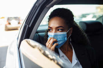 Fototapeta na wymiar Young businesswoman being a taxi passenger and having a ride wearing and adjusting medical mask for health protection. Business trips during pandemic, new normal and coronavirus travel safety concept.