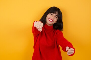Caucasian brunette woman wearing red casual sweater isolated over yellow background  imagine steering wheel helm rudder passing driving exam good mood fast speed