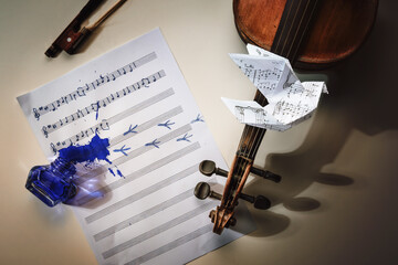Violin and a sheet of music with started handwritten song All the birds are already here, overturned ink jar, bird footprints and an origami dove flying away, misfortune of a composer concept