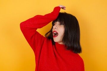 Caucasian brunette woman wearing red casual sweater isolated over yellow background surprised with...