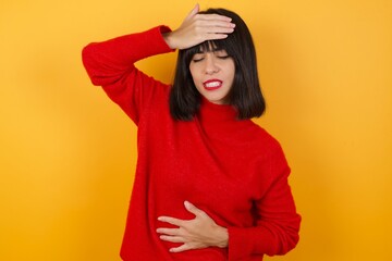 Caucasian brunette woman wearing red casual sweater isolated over yellow background Touching forehead for illness and fever, flu and cold, virus sick.