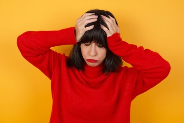 Caucasian brunette woman wearing red casual sweater isolated over yellow background suffering from strong headache desperate and stressed because of overwork. Depression and pain concept.