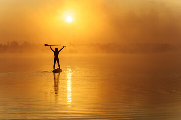 Strong man standing on sup board with paddle above head