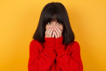 Vivacious Caucasian brunette woman wearing red casual sweater isolated over yellow wall, giggles...