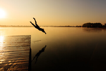 Active man jumping from wooden pier at foggy lake