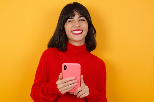 Caucasian brunette woman wearing red casual sweater isolated over yellow background taking a selfie  celebrating success