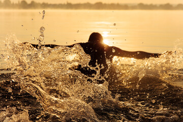 Strong man in silhouette swimming at lake in butterfly style