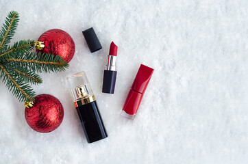 decorative luxury cosmetics, red lipstick, nail polish, perfume under spruce branch with balls in...