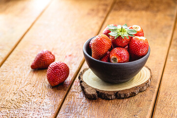 Pile of fresh Brazilian strawberries in a ceramic bowl on rustic wooden background.