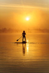 Silhouette of man swimming on sup board in early morning
