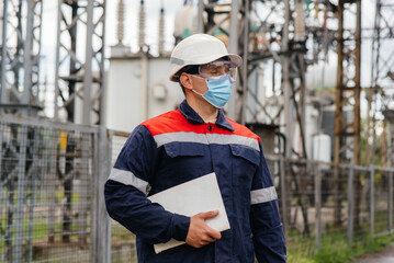 An electrical substation engineer inspects modern high-voltage equipment in a mask at the time of pondemia. Energy. Industry