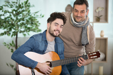 mid-adult man teaching a young man during a guitar lesson