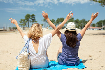 rear view of two woman on beach with arms raised