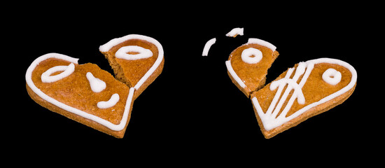 Two broken gingerbreads in heart shape with painted smiley isolated on black background. Close-up of cracked baked holiday pastries decorated by smiling and sad emoticon. Damaged aromatic Xmas sweets.