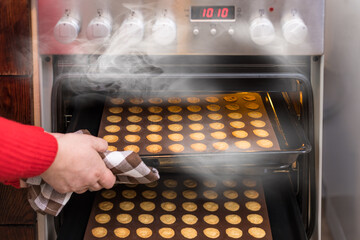 Hand taking hot nutty cookies out of a steaming convection oven of kitchen stove. Fresh baked...