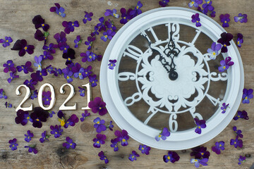 The numbers 2021 are next to a large white clock showing the five minutes of the new year, next to a lot of purple Pansy Flowers.