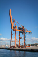 Huge orange crane in a harbour, blue sky, few clouds.