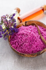 Sea salt in bowl, aroma oil in bottles, Wellness and flowers on grey textured background and flowers on vintage wooden background. Selective focus.