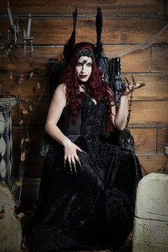 A Woman wearing a winged headdress sits in a black gothic throne in a Halloween themed image