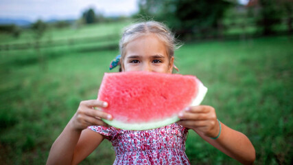 Healthy summer food. Cute kid biting a slice of watermelon in the backyard of farmhouse
