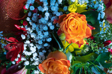 A beautiful composition of wildflowers and orange roses rests on a wooden chair. Close up shot: dew drops are recognized.