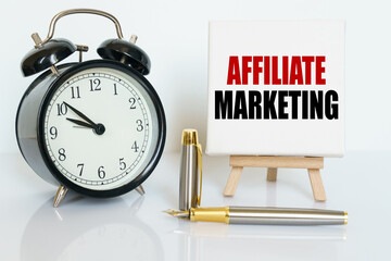 On the table there is a clock, a pen and a stand with a card on which the text is written - AFFILIATE MARKETING.