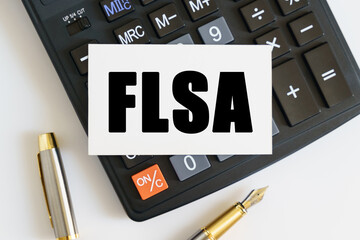 On the table there is a pen, a calculator and a business card on which the text is written FLSA. FAIR LABOR STANDARDS ACT
