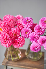 Lilac and pink dahlias in glass jug, neutral wall background. the work of the florist at a flower shop. Handsome fresh bouquet. Flowers delivery