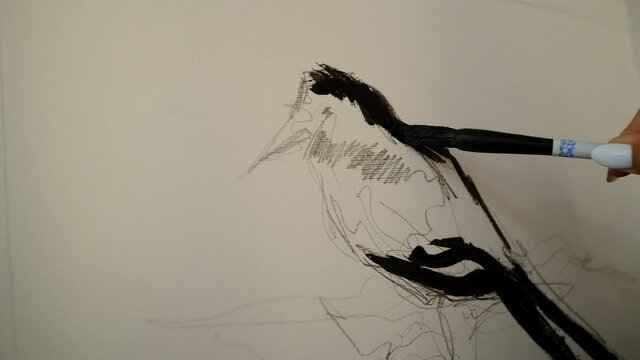 Girl draws a magpie bird on a white canvas with a pencil