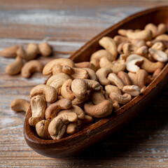 Pile of roasted cashew nuts in a wooden bowl, top close up view